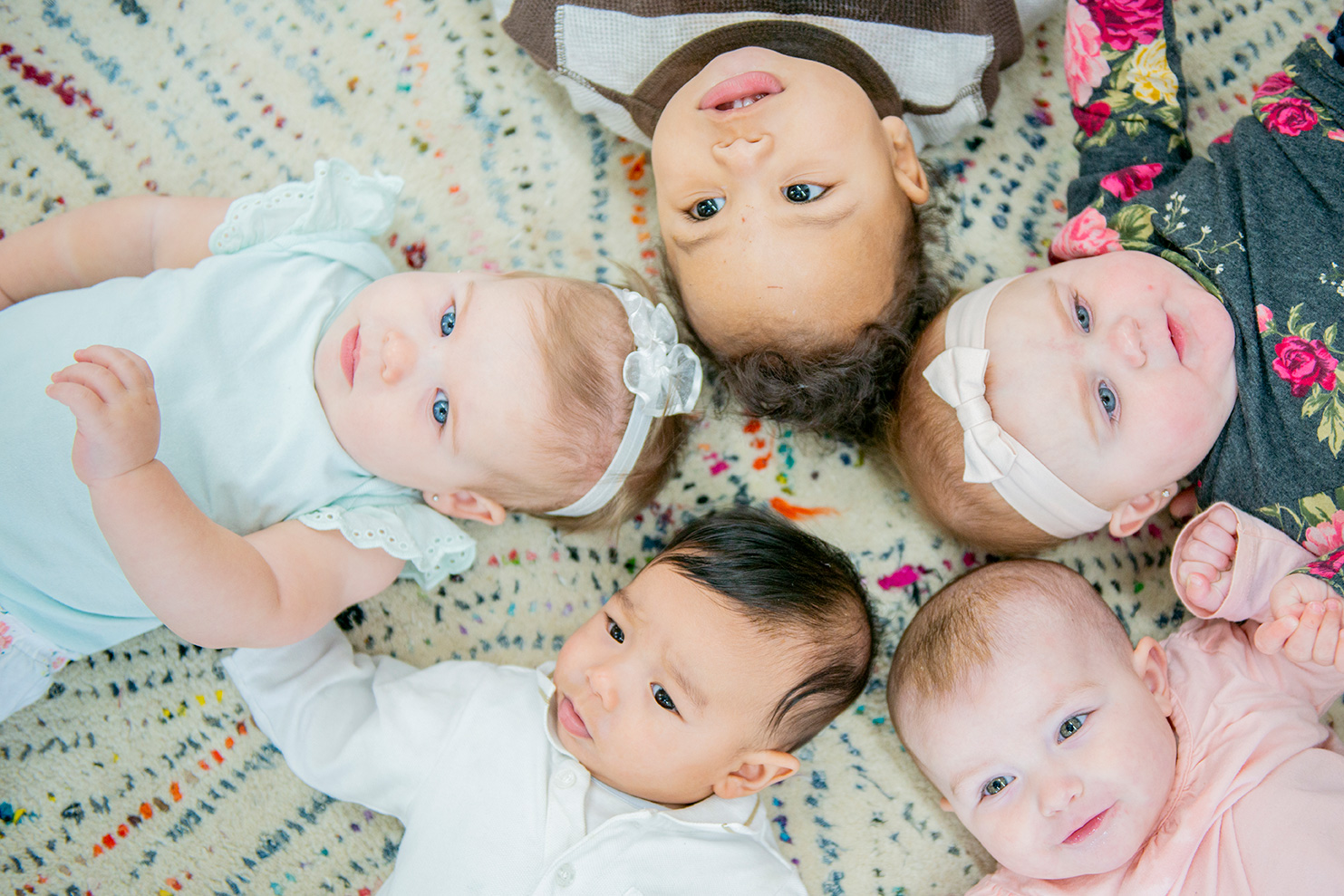 A group of babies are in a daycare centre. They are lying in a circle with their heads touching.
