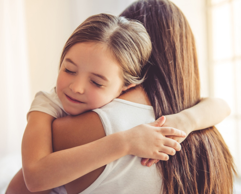 Beautiful young woman and her charming little daughter are hugging and smiling