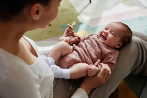 High angle view at cheerful newborn lying on knees of mom holding baby hands at home